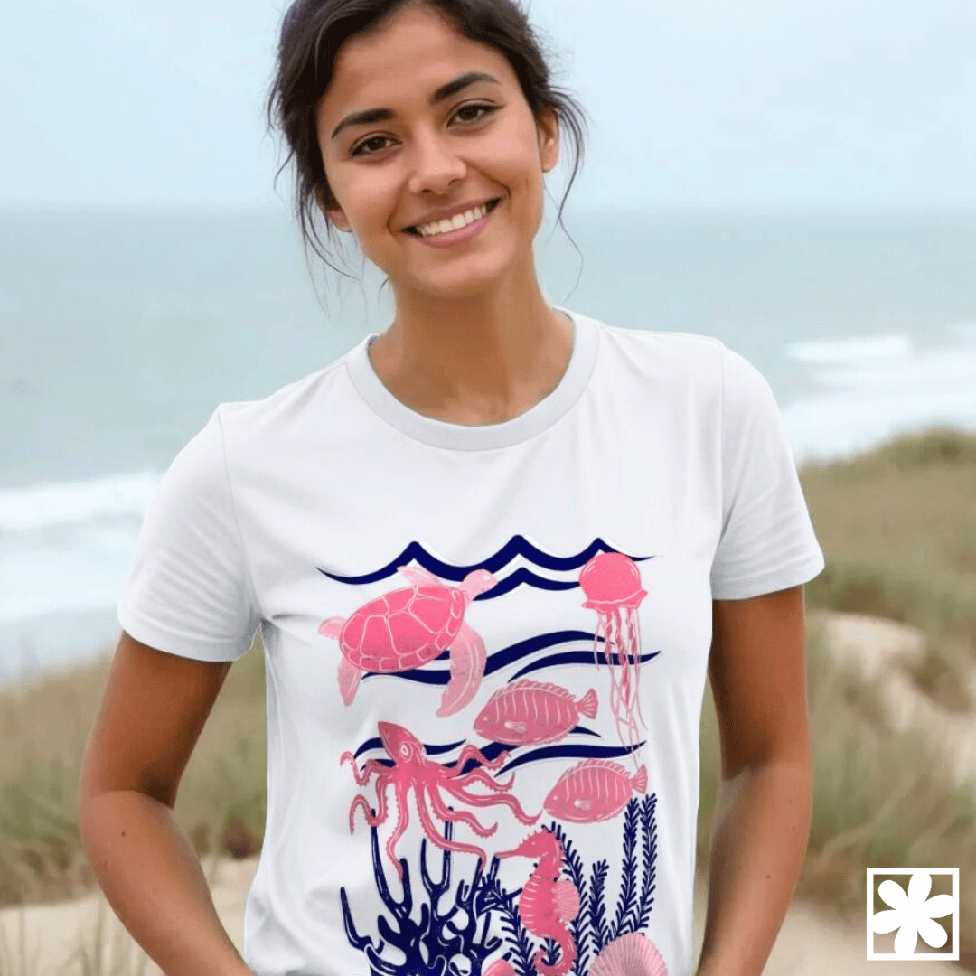 A woman stands on the beach with an ocean themed T-shirt full of sea creatures.