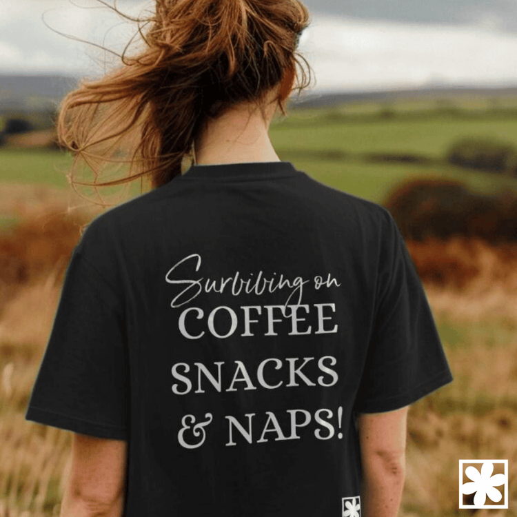 A woman faces away from the camera and on the back of her slogan t-shirt is the phrase "surviving on coffee, snacks and naps!"